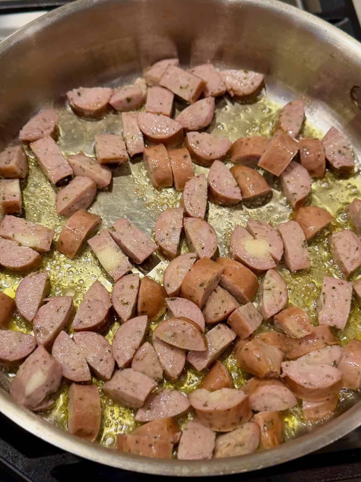 Sliced sausage browning in olive oil in a large pan.