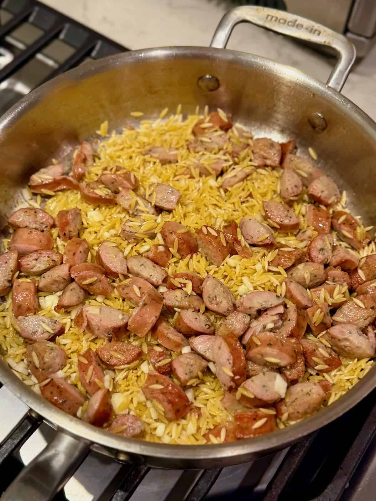 Browned sausage, orzo, and garlic cooking together in a pan.