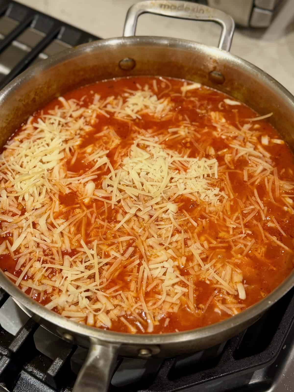 Sausage and orzo covered with tomato sauce and shredded cheese before baking.