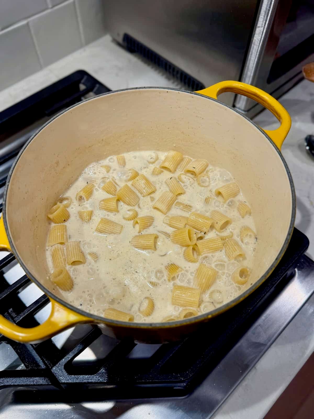 Mezzi rigatoni pasta cooks in a seasoned milk and broth mixture.