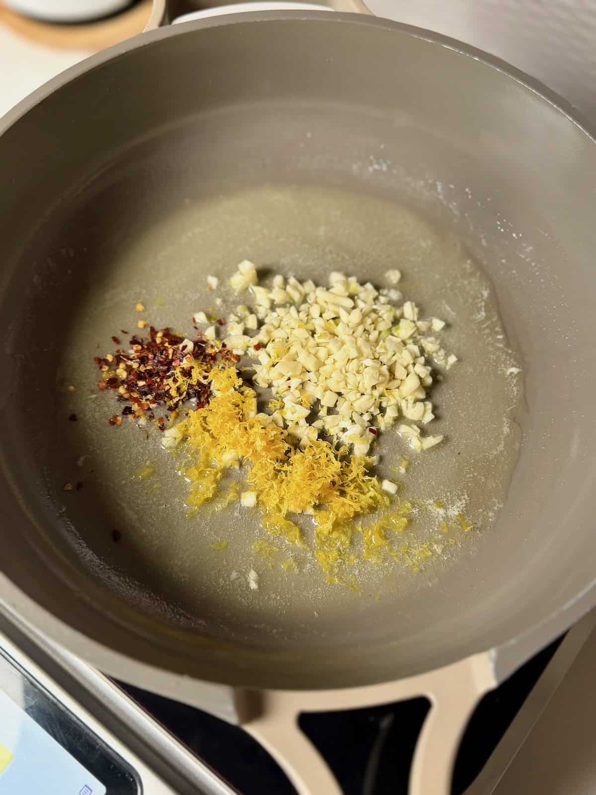 Garlic, lemon zest, and red pepper flakes cooking in melted butter in a skillet.