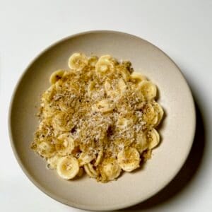 A bowl of lemon garlic orecchiette topped with brown butter breadcrumbs and grated parmesan cheese.