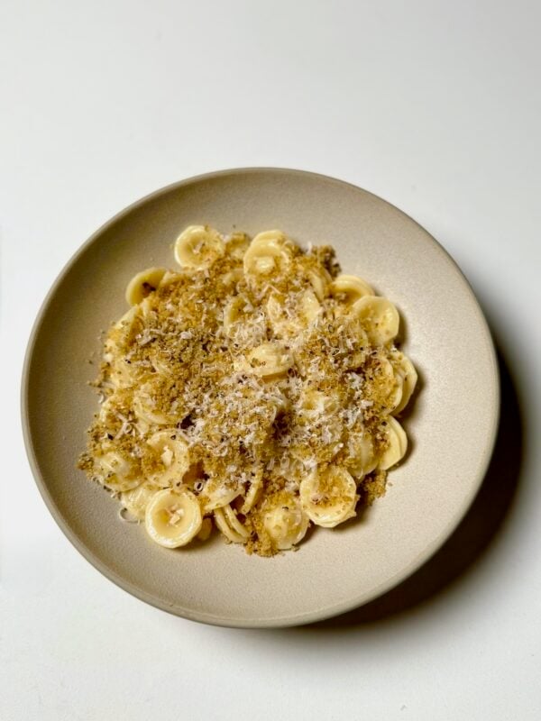 A bowl of lemon garlic orecchiette topped with brown butter breadcrumbs and grated parmesan cheese.