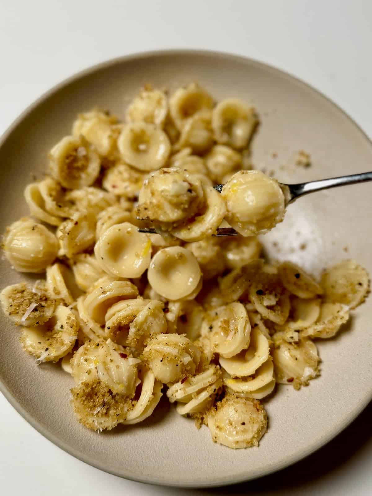 A fork lifting orecchiette coated in lemon butter sauce with brown butter breadcrumbs.