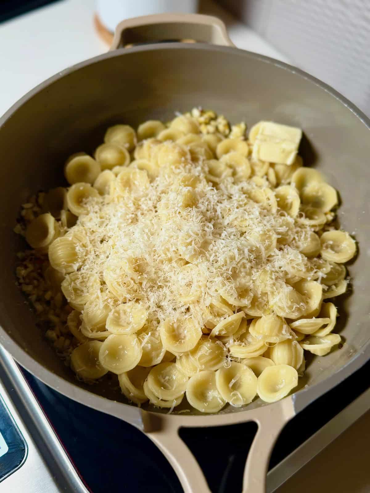 Cooked orecchiette pasta added to a skillet with garlic and lemon butter.