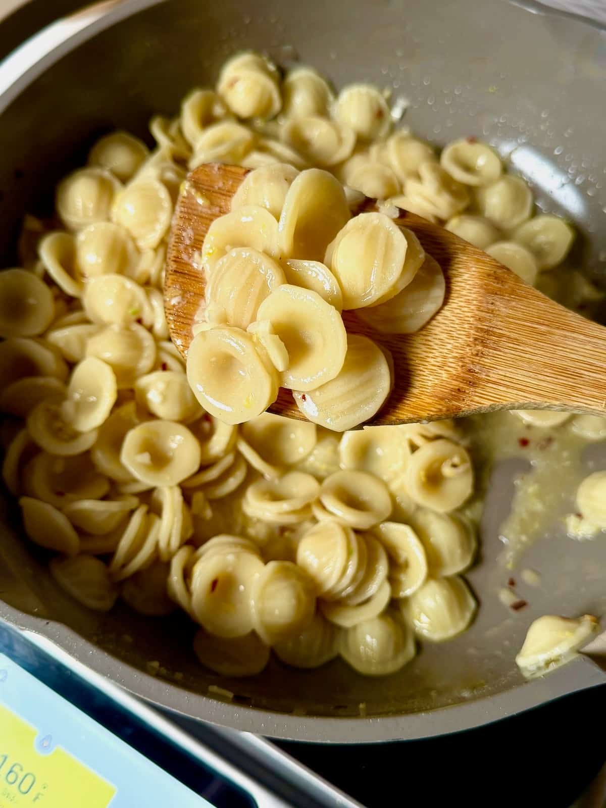 Orecchiette coated in lemon garlic butter sauce on a wooden spoon.