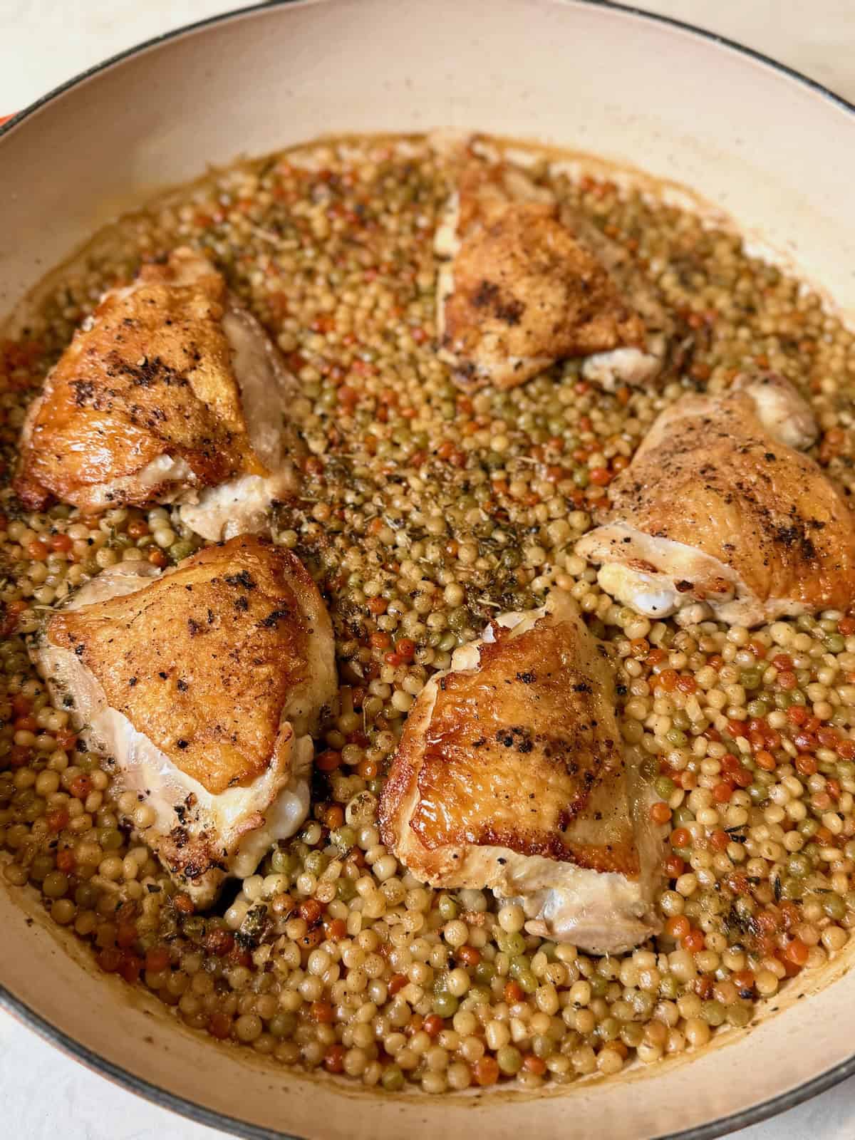 Crispy chicken thighs baked over lemon couscous in a large braiser.