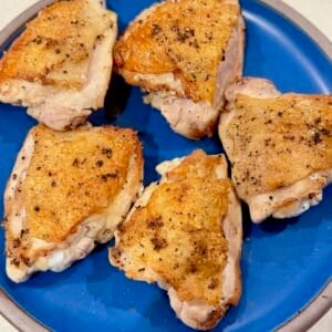Golden crispy chicken thighs resting on a plate after searing.