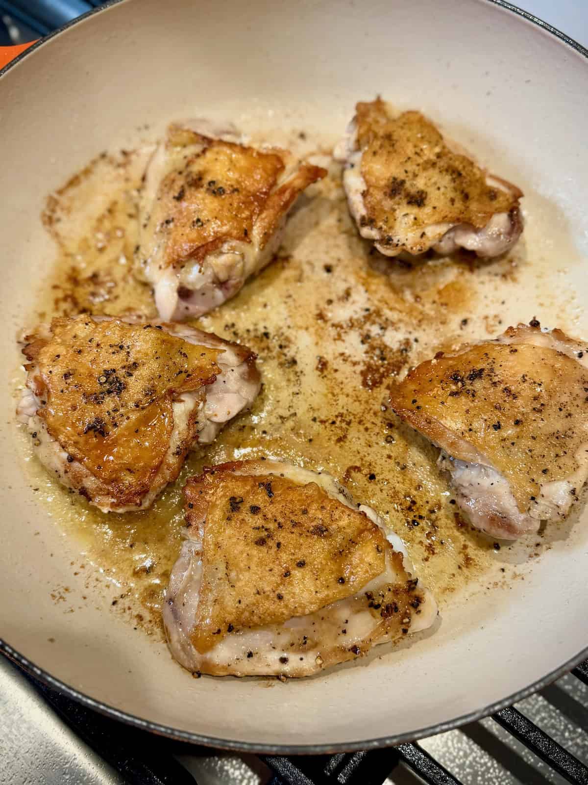 Chicken thighs searing skin-side up after crisping the skin.