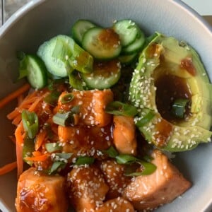 A grey bowl with salmon, avocado, cucumber, and sauce