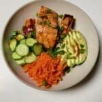 A teriyaki salmon bowl with rice, avocado, cucumber, shredded carrots, and cooked salmon arranged in sections.