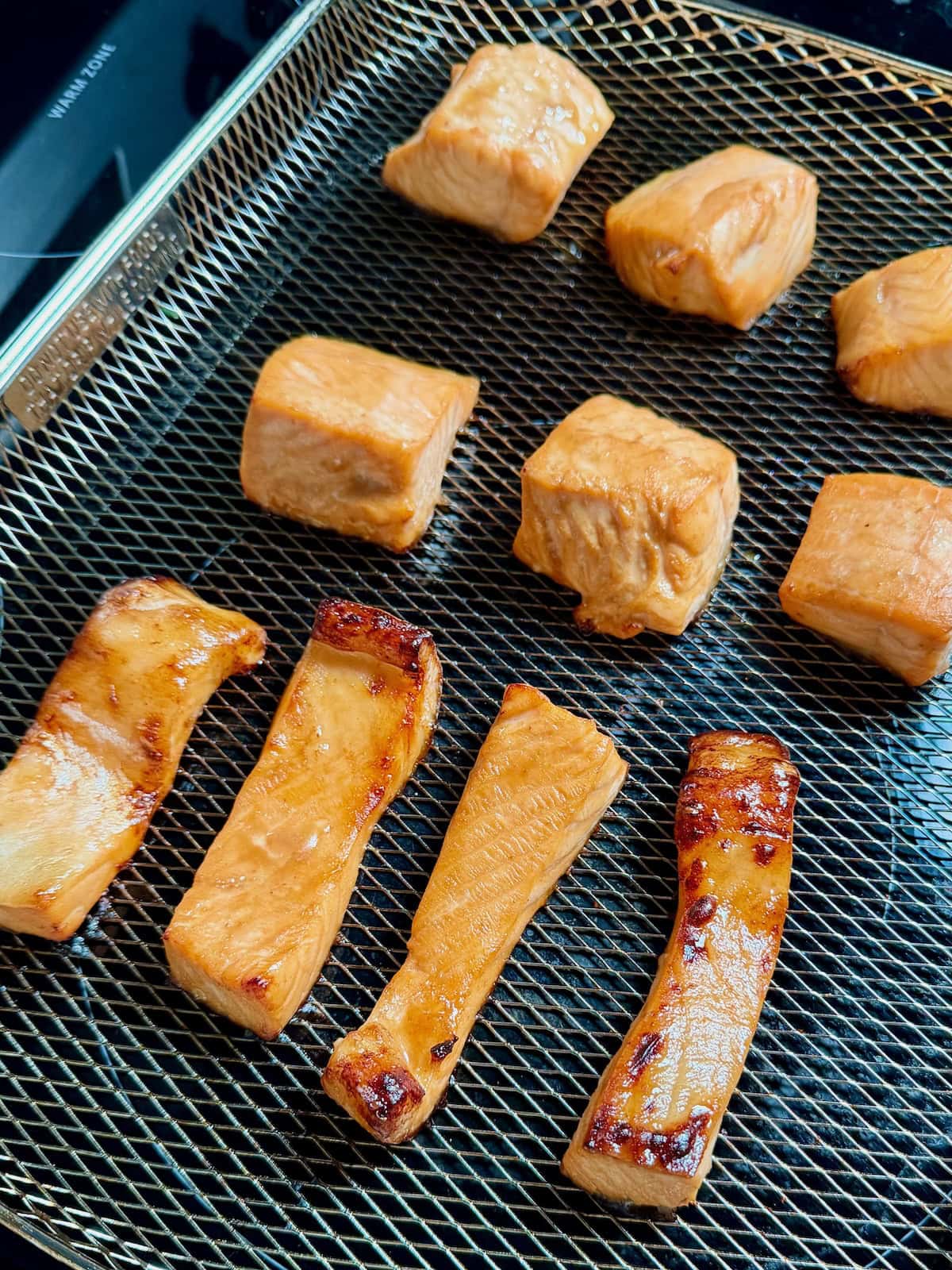Cooked teriyaki salmon pieces in an air fryer basket with slightly caramelized edges.