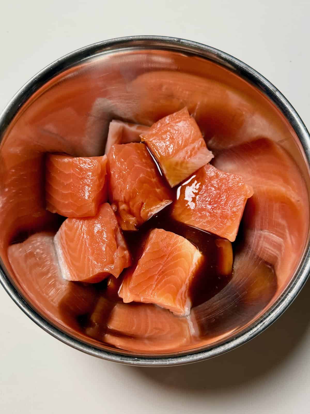 Cubed salmon coated in teriyaki sauce in a bowl, ready to marinate before cooking.