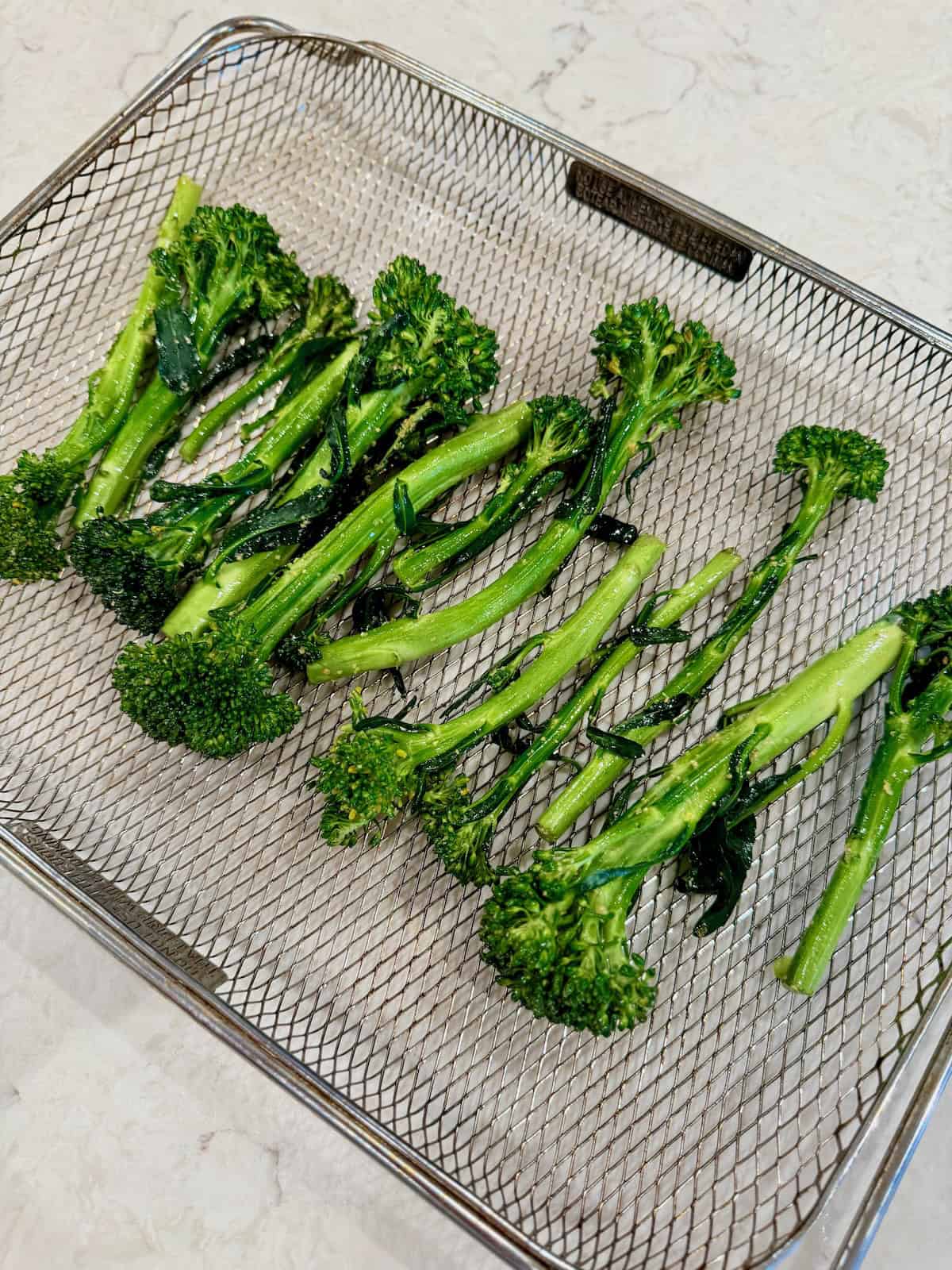 Seasoned baby broccoli is arranged in a single layer in the air fryer basket.