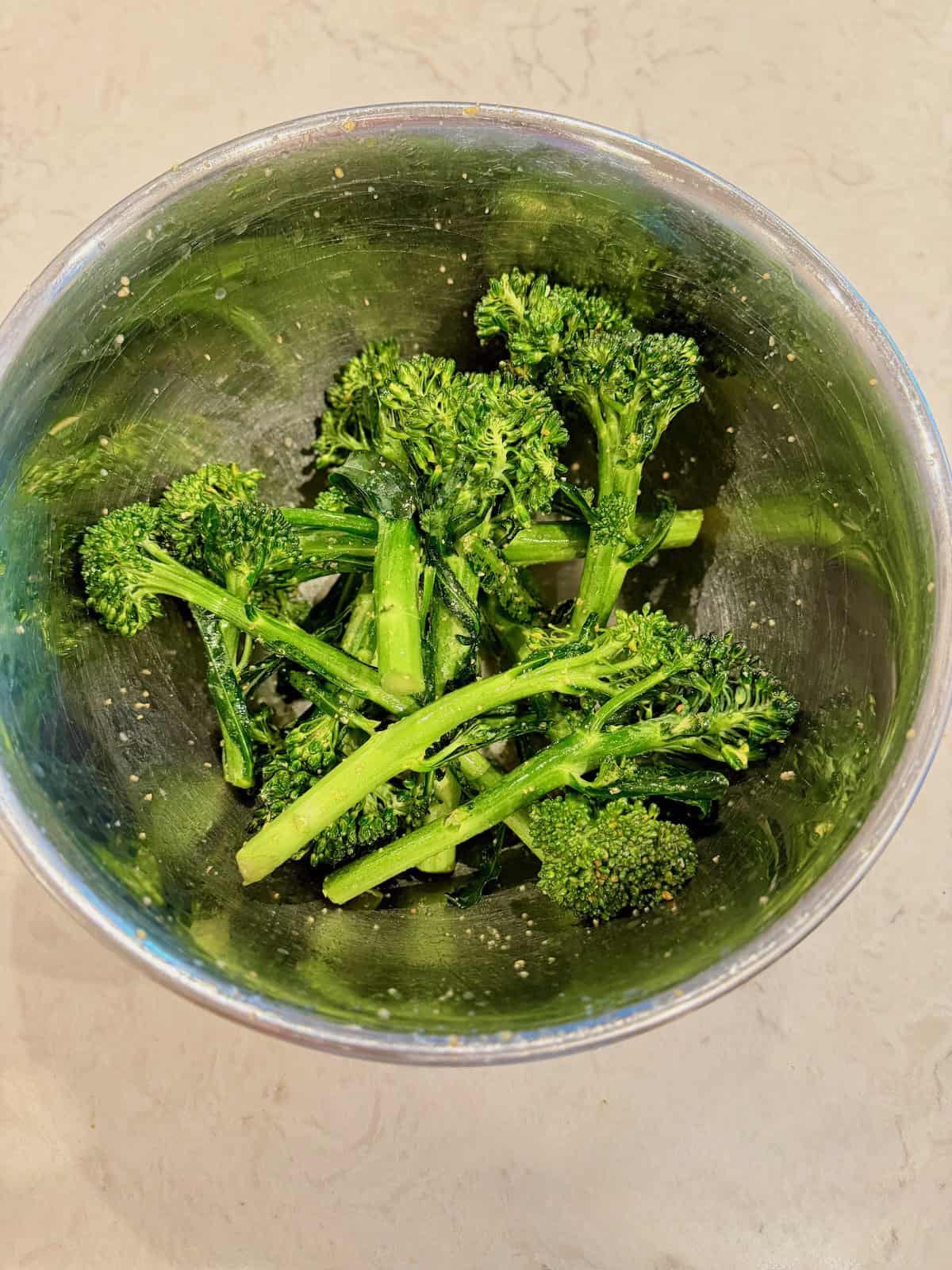 Fresh baby broccoli is tossed with olive oil and seasonings in a bowl.