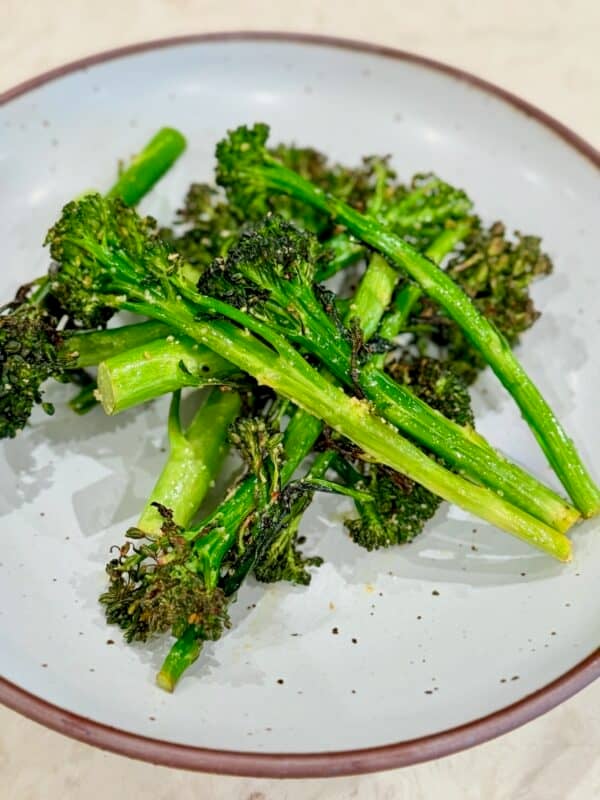 Air fried baby broccoli is served in a bowl with browned, crispy edges.