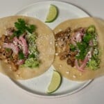 Instant Pot Mexican Chicken inside a tortilla with cilantro, cheese, pickled red onions, and limes