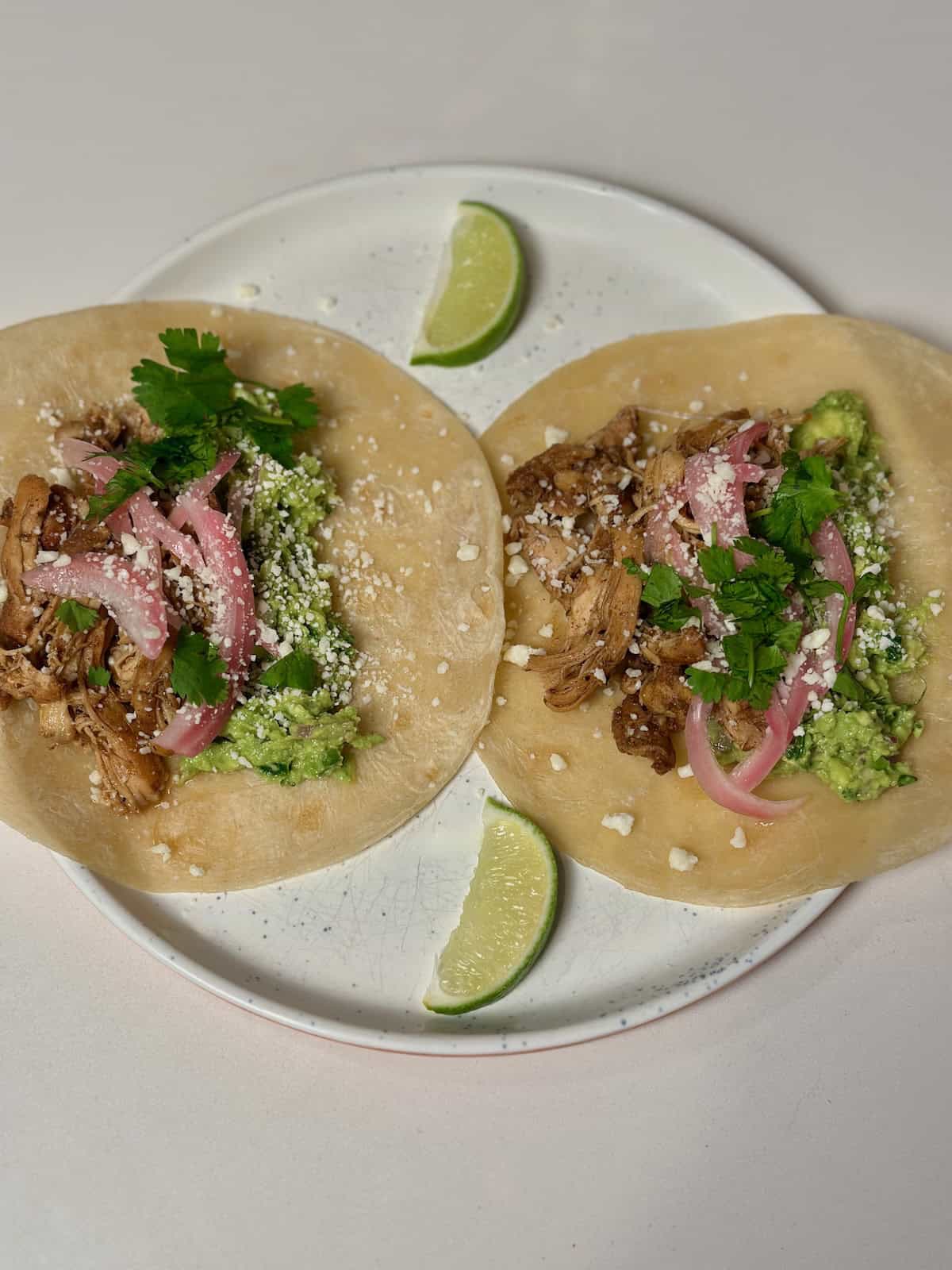 Instant Pot Mexican Chicken inside a tortilla with cilantro, cheese, pickled red onions, and limes