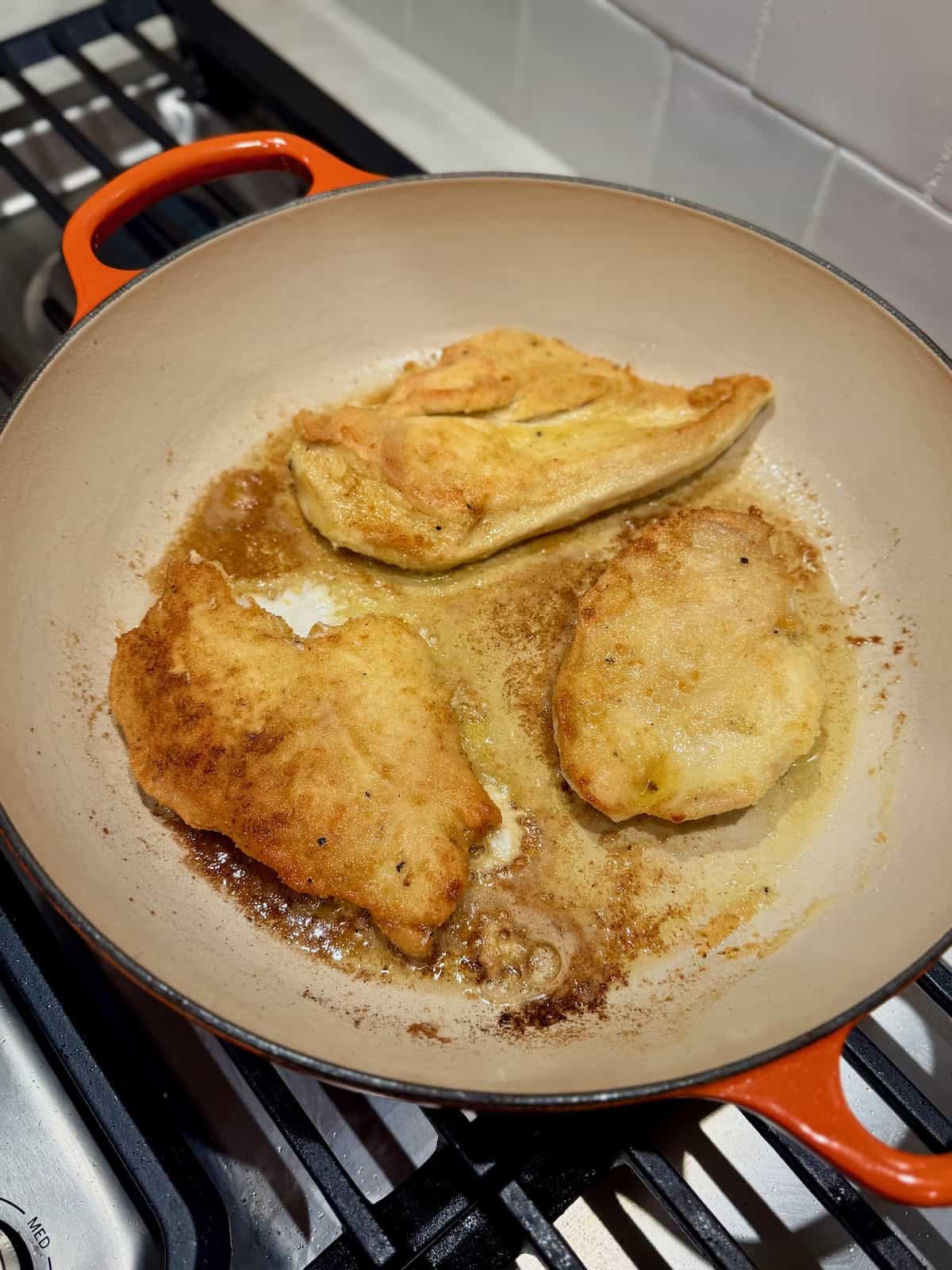 Flour-coated chicken cutlets cook in a skillet until golden brown.