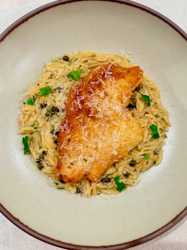 Golden chicken piccata is served over creamy lemon caper orzo with fresh parsley.