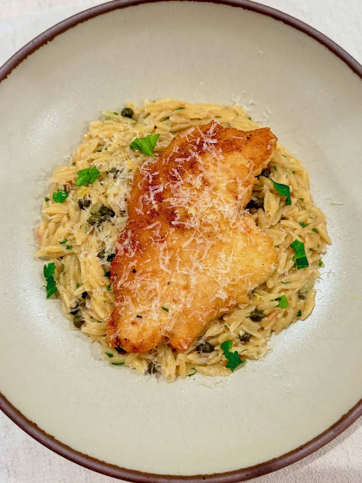 Golden chicken piccata is served over creamy lemon caper orzo with fresh parsley.