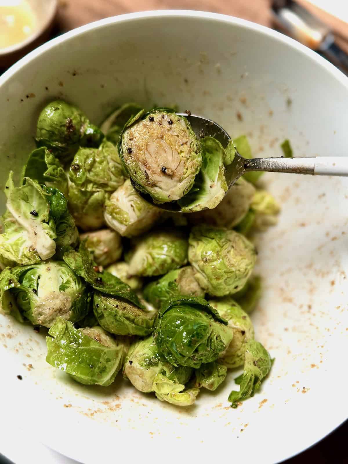 Brussels Sprouts tossed with seasonings in a bowl.