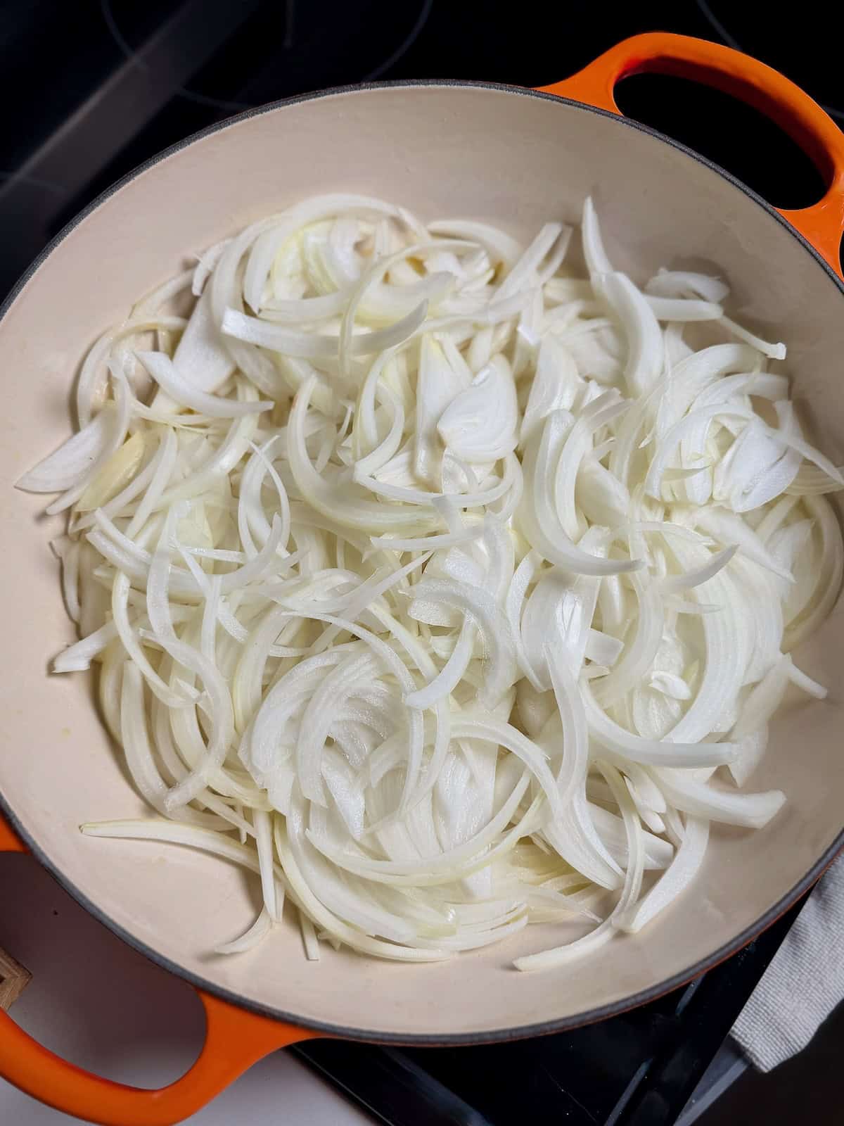 Thinly sliced onions in a pan before caramelizing.