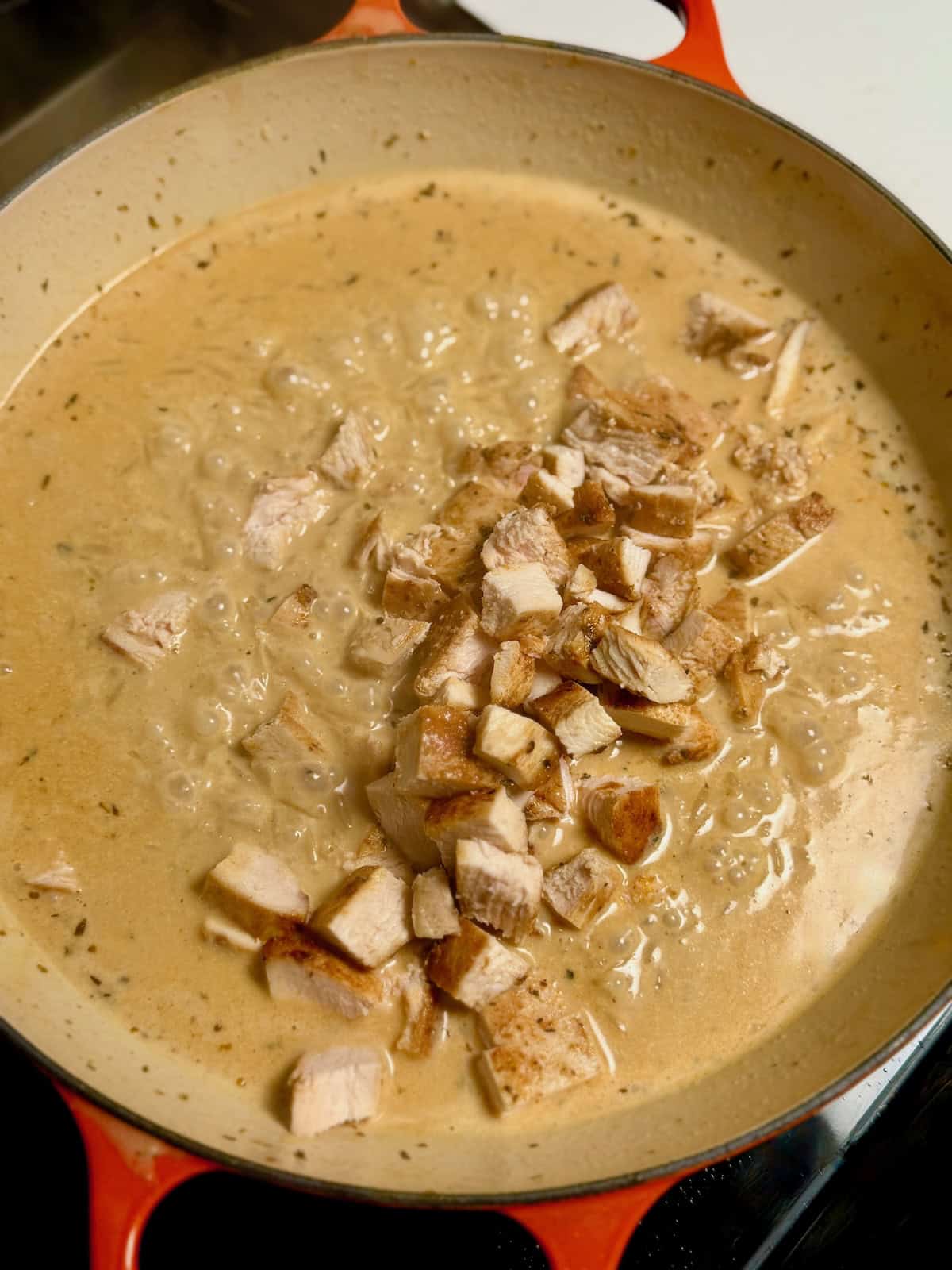Chopped Cajun chicken added to creamy Alfredo orzo sauce in a skillet.