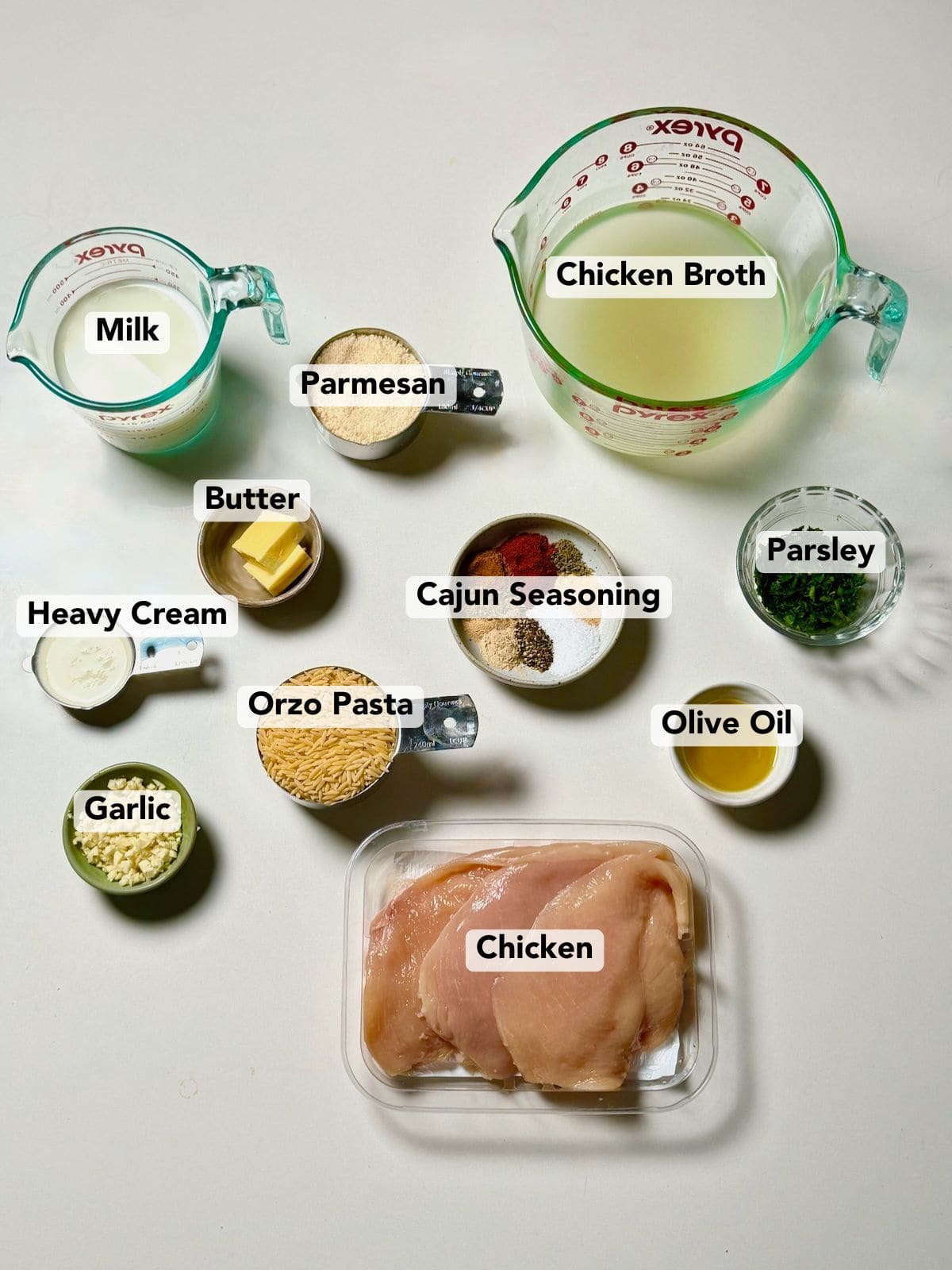 Ingredients for Cajun chicken Alfredo orzo including chicken, orzo, Cajun seasoning, garlic, cream, broth, Parmesan, butter, and parsley.