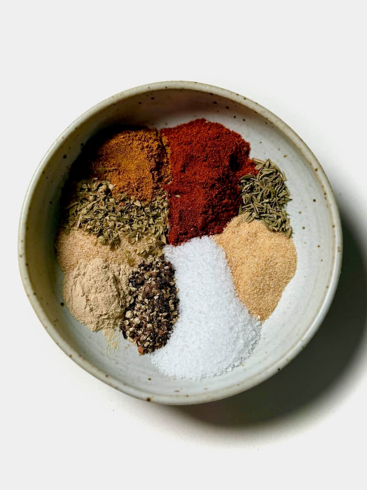 A bowl of homemade Cajun seasoning with paprika, garlic powder, onion powder, oregano, thyme, salt, and black pepper.