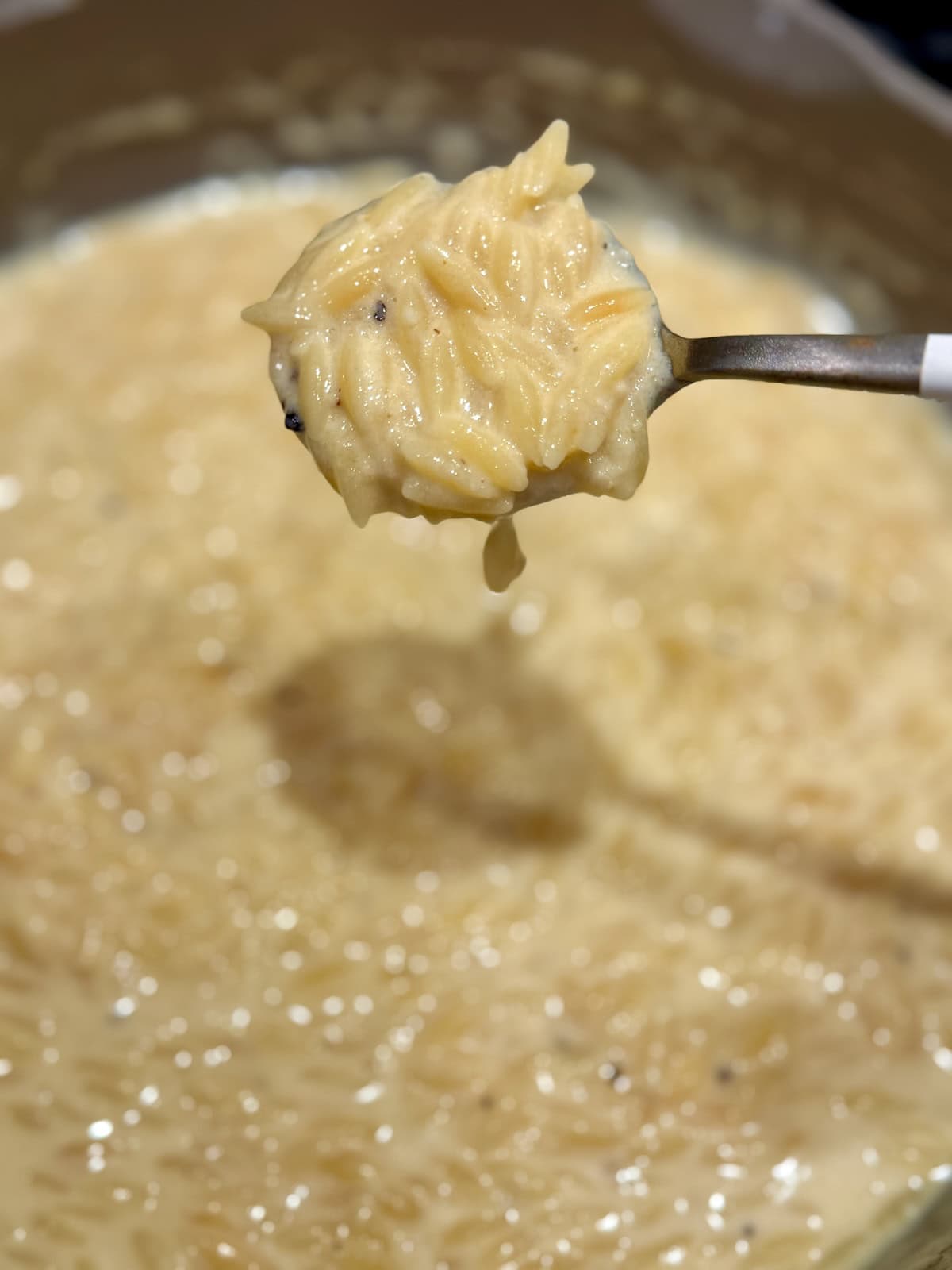 A spoonful of creamy orzo mac and cheese is held above the finished skillet.