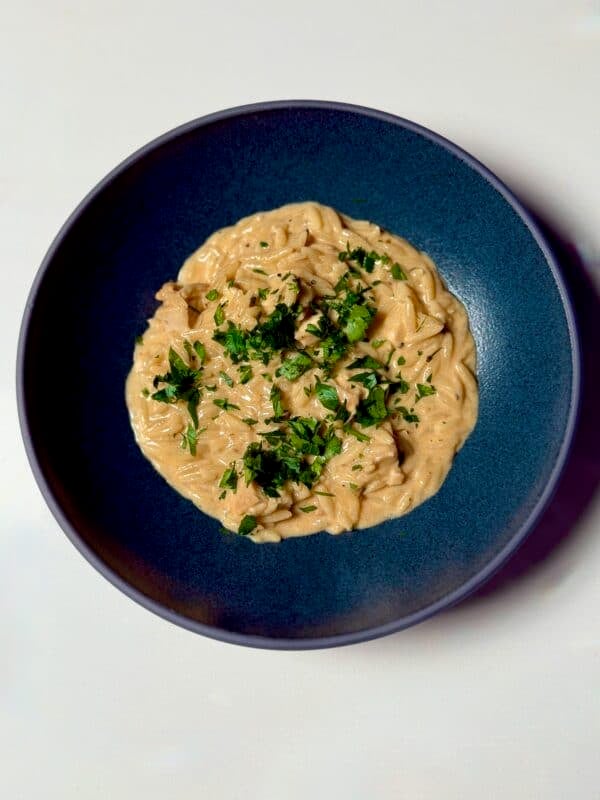 Creamy Cajun chicken Alfredo orzo garnished with fresh parsley in a blue bowl.