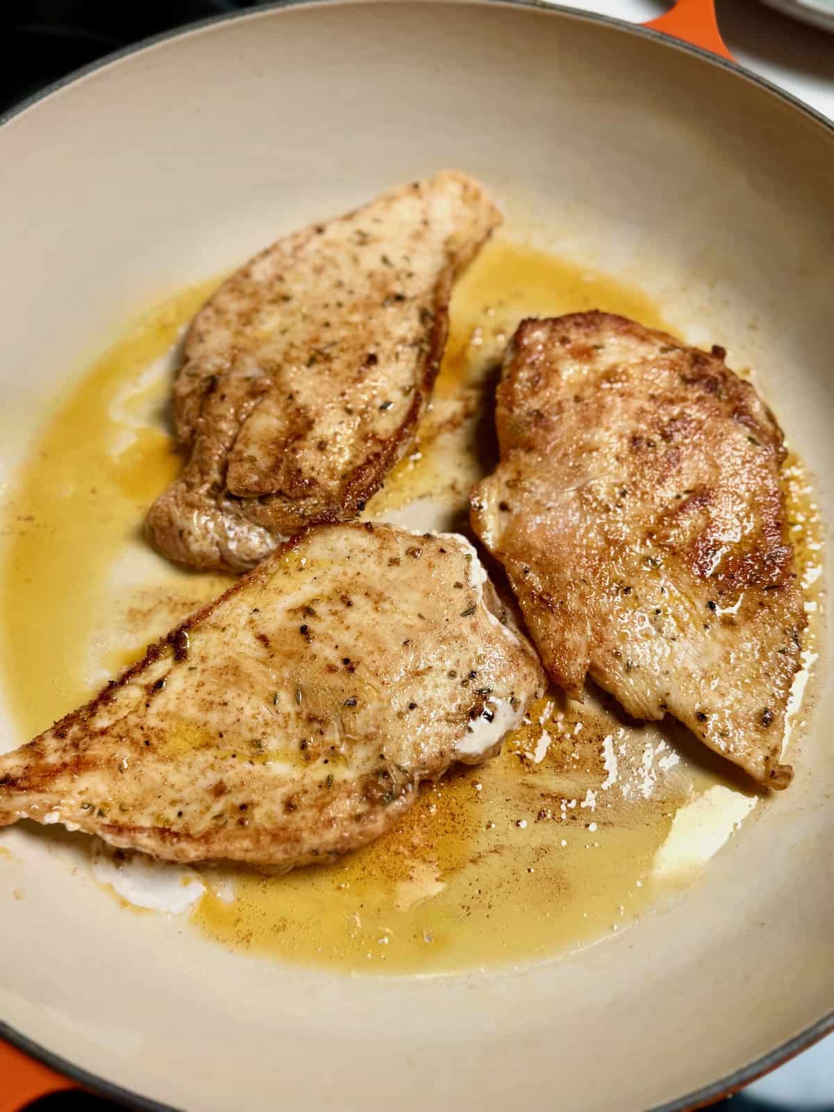 Cajun seasoned chicken cooking in a skillet with butter and oil.
