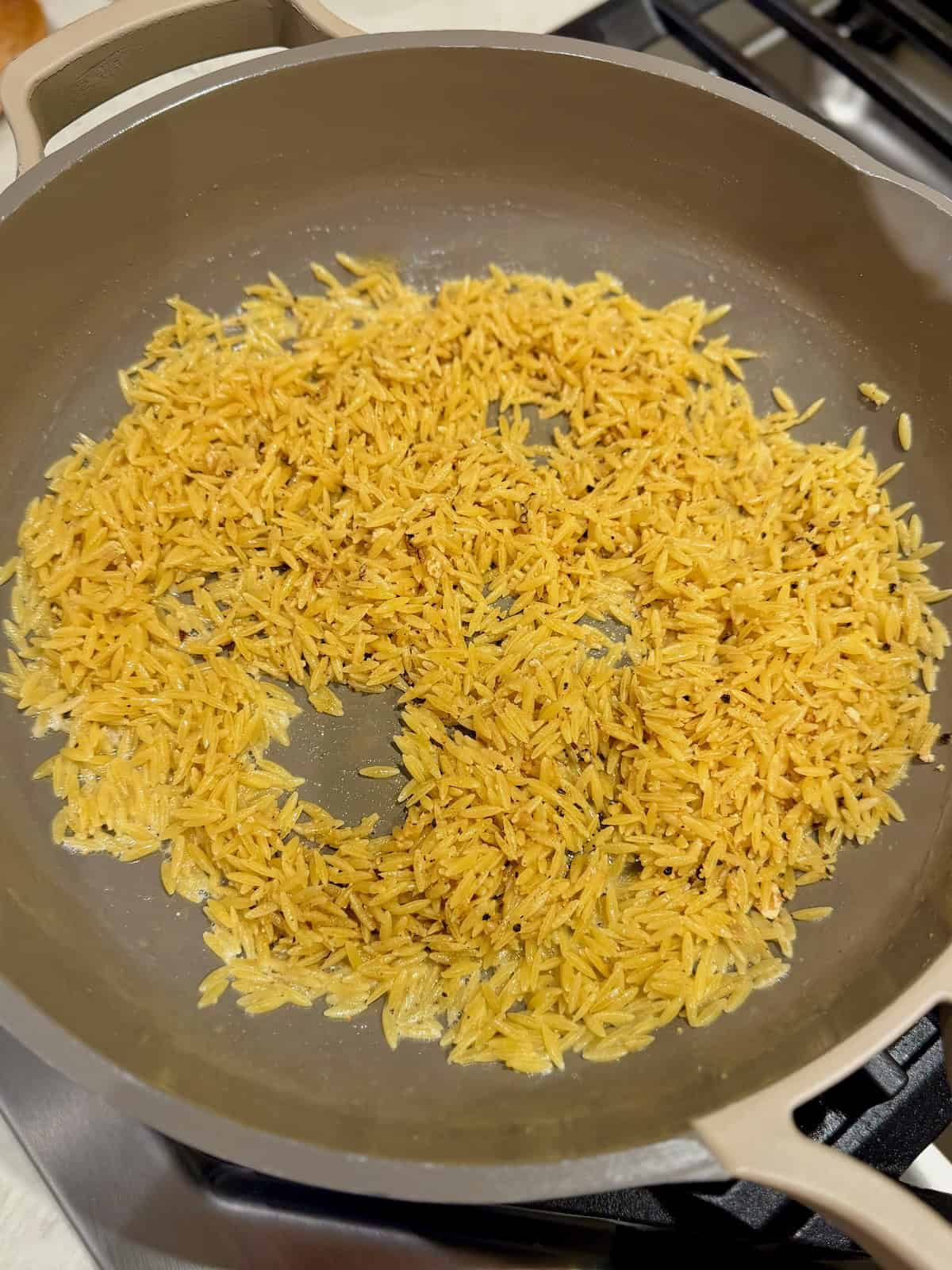 The orzo is toasted in a skillet with butter and seasonings until golden.