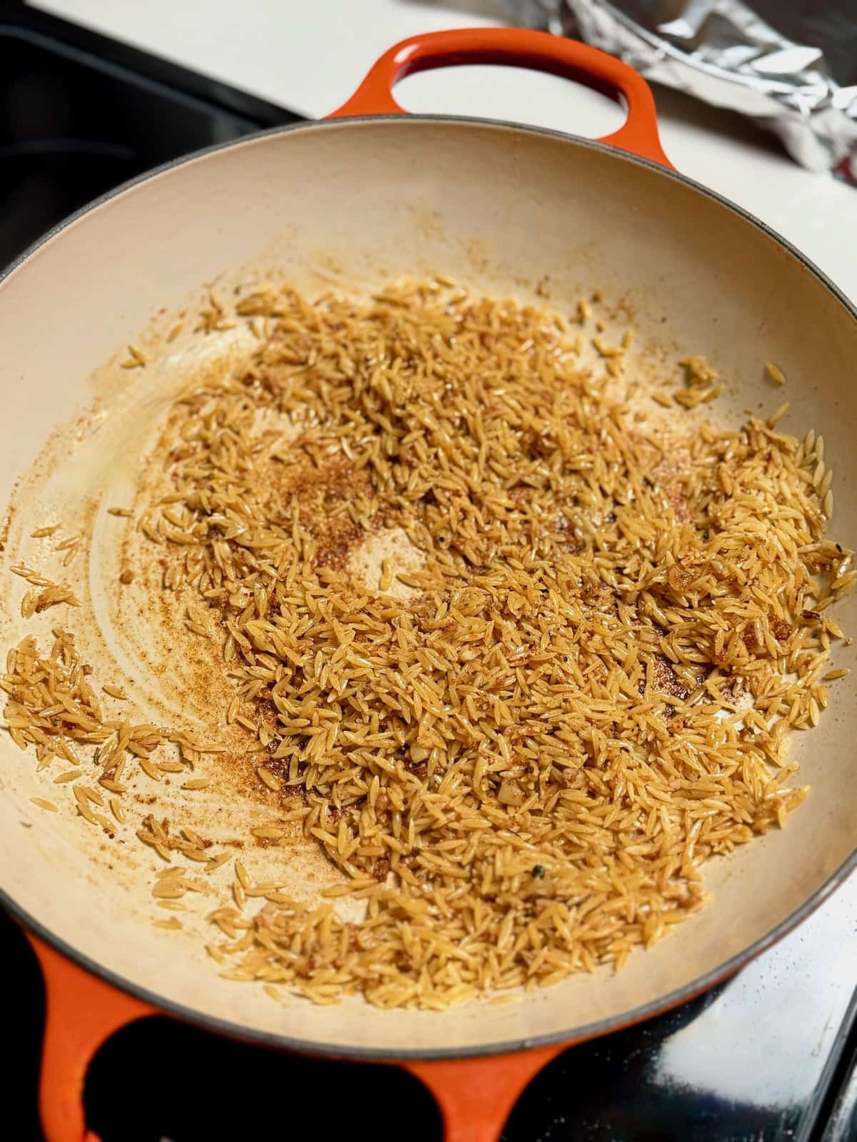 Orzo pasta toasting in butter and garlic in a skillet.