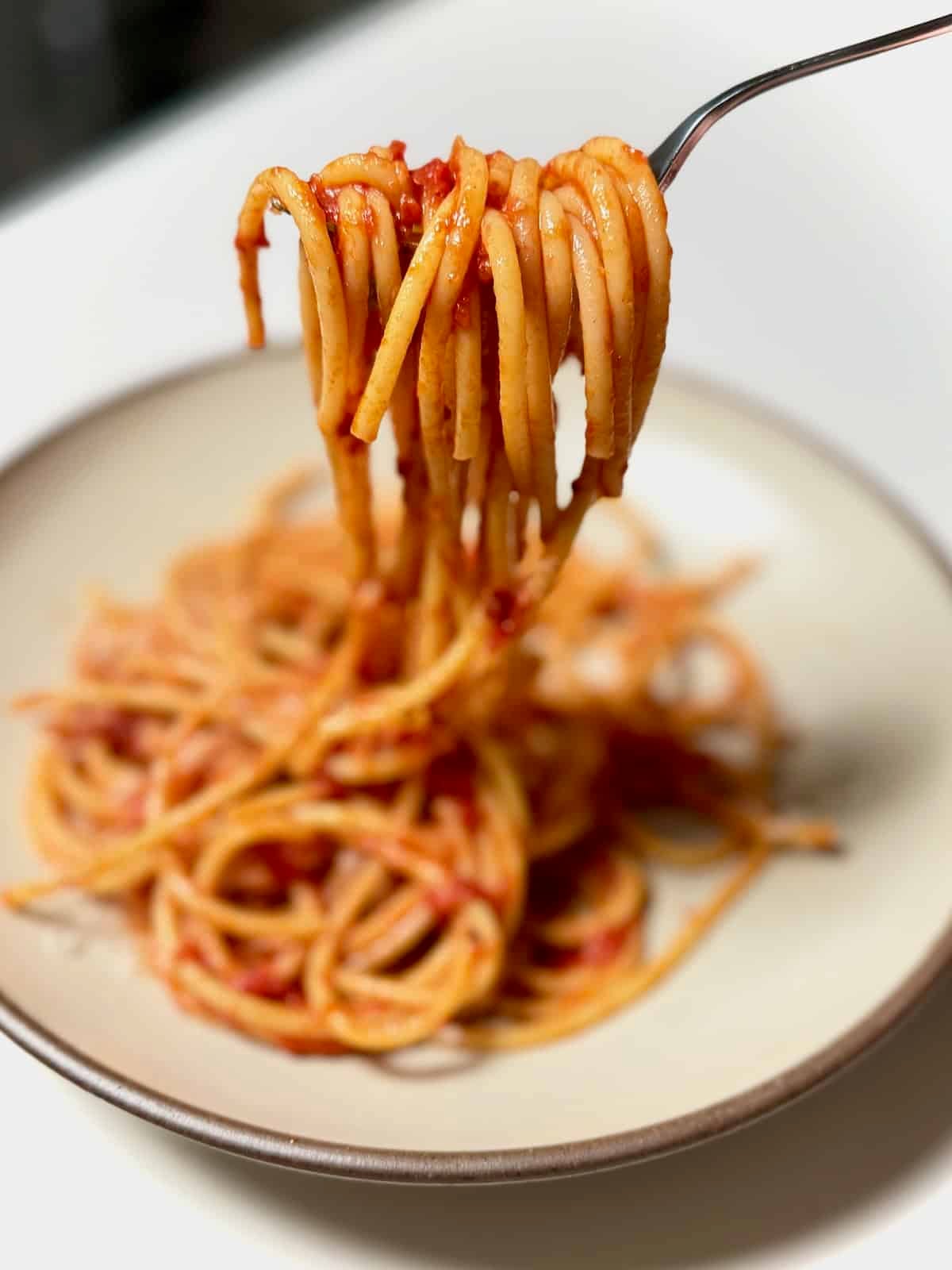 Fork twirling bucatini amatriciana with bowl underneath.
