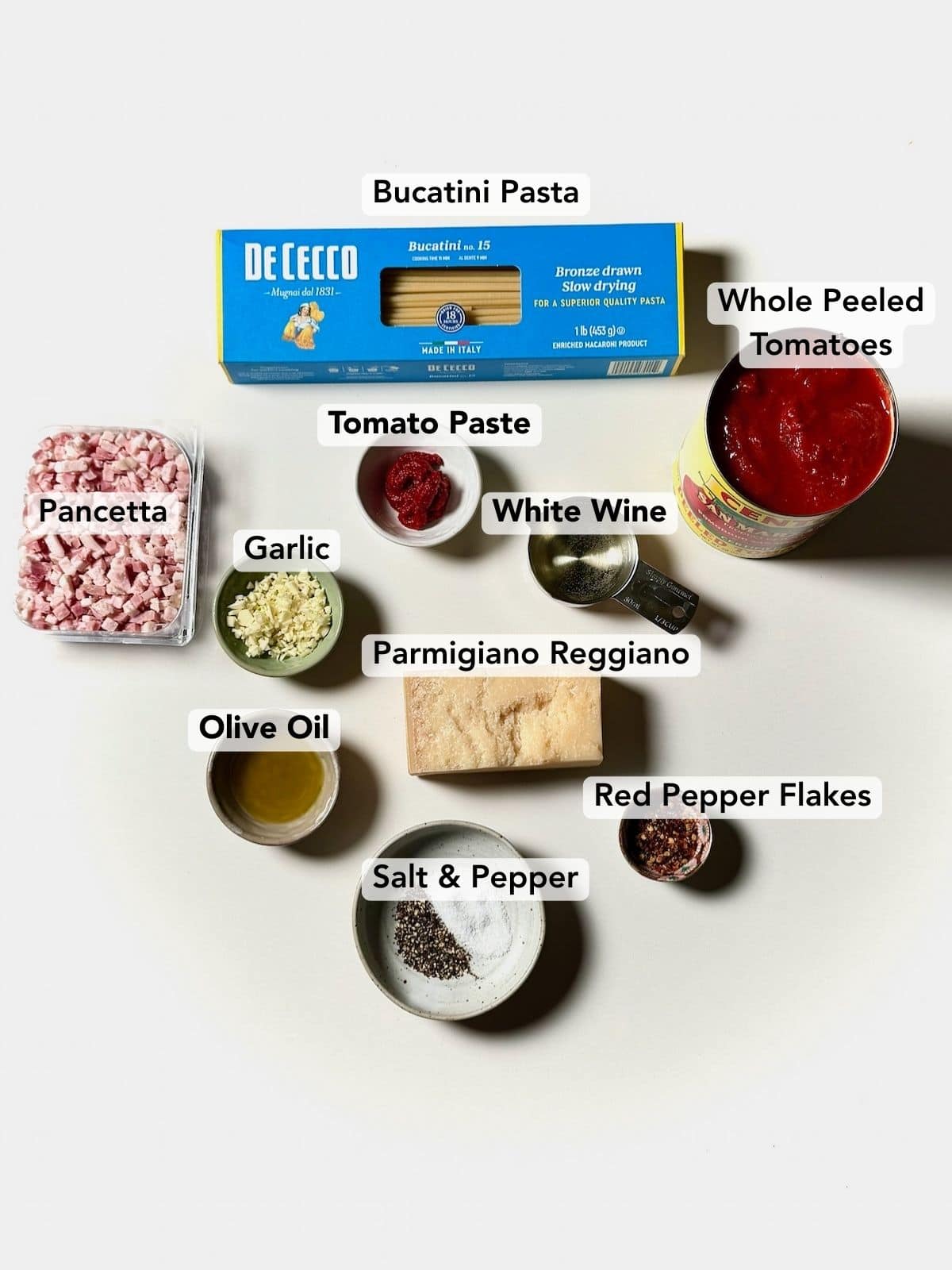 Ingredients for bucatini amatriciana including pancetta, tomatoes, bucatini, garlic, olive oil, and pecorino cheese.