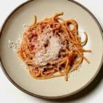Plated bucatini amatriciana topped with grated cheese.