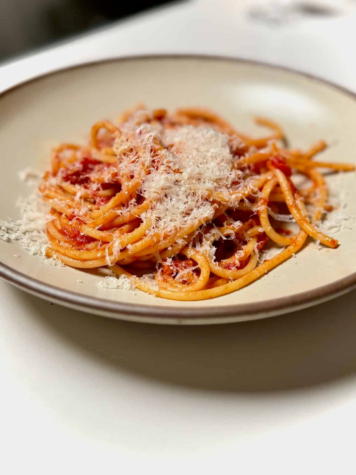 Plated bucatini amatriciana topped with grated cheese in white bowl.