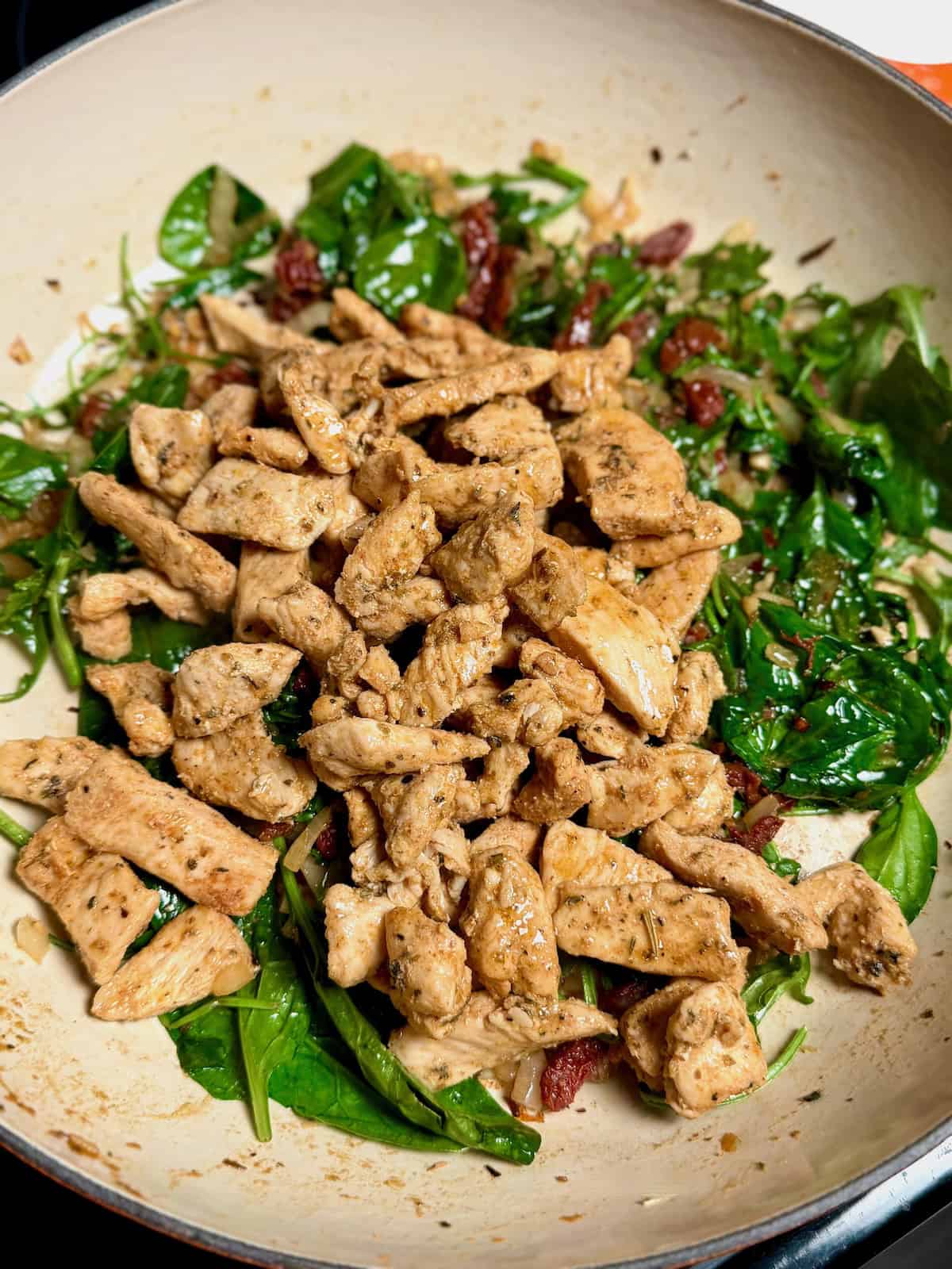 Cooked chicken mixed with spinach and sun-dried tomatoes in a pan.