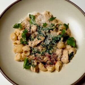 A bowl of creamy sun-dried tomato chicken pasta topped with Parmesan cheese and fresh herbs.