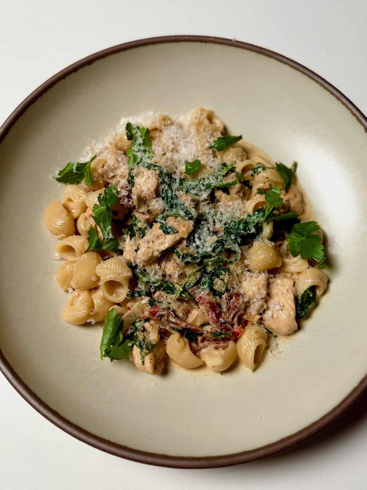 A bowl of creamy sun-dried tomato chicken pasta topped with Parmesan cheese and fresh herbs.
