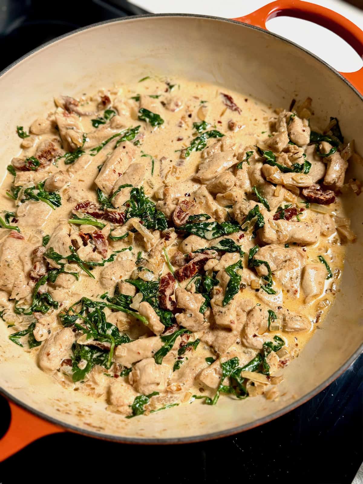 Creamy sun-dried tomato sauce with chicken and spinach simmering in a pan before adding pasta.