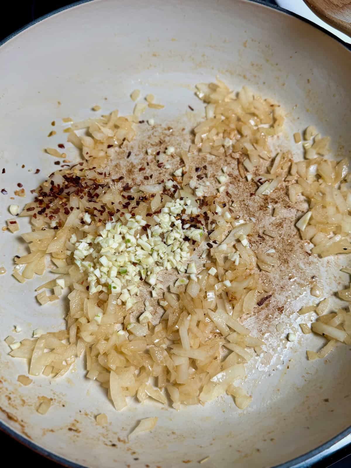 Onions, garlic, and sun-dried tomatoes sautéing in a pan to build the flavor base for the pasta sauce.