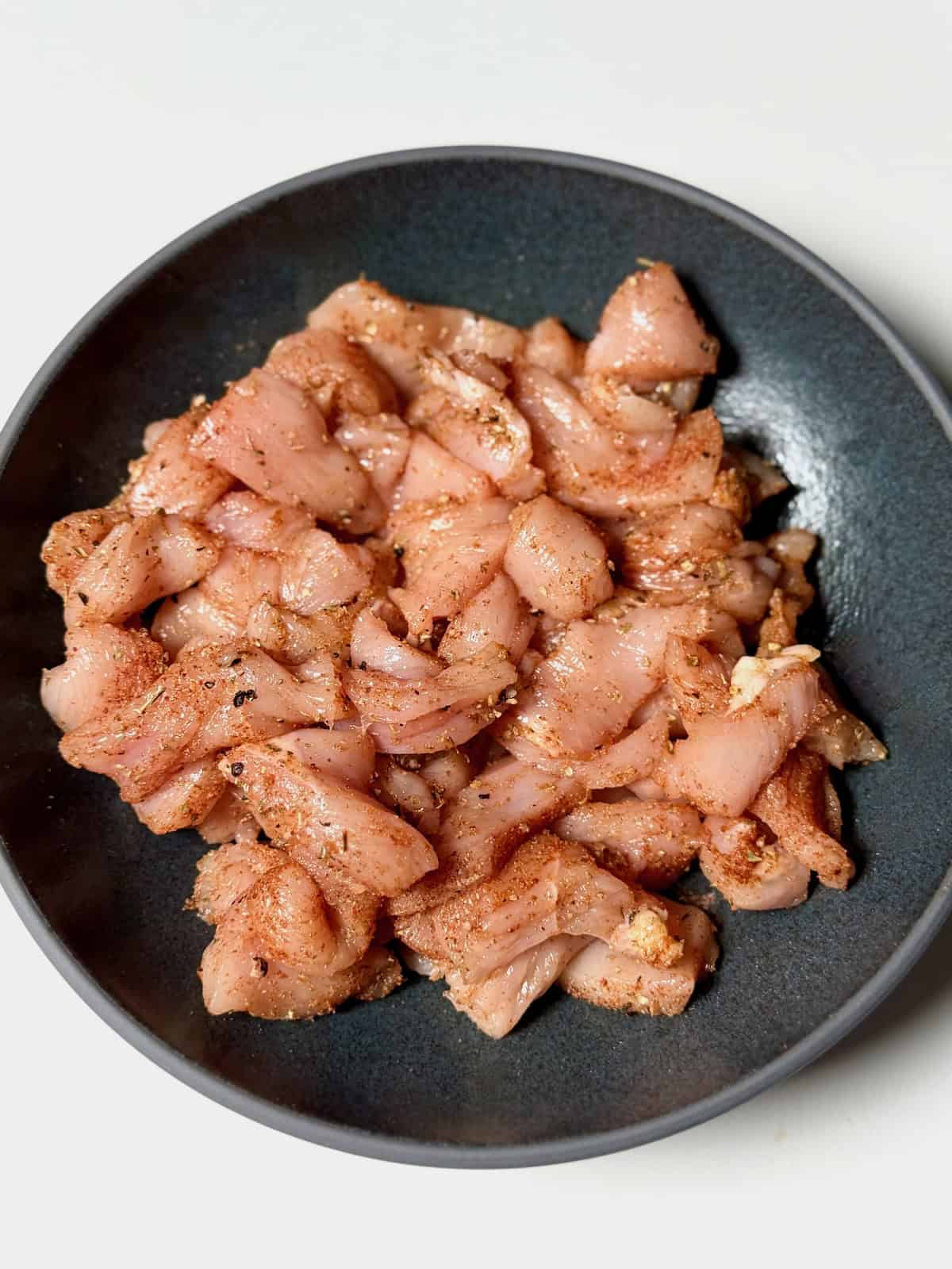 Cubed chicken seasoned with spices in a bowl, ready to be cooked for creamy sun-dried tomato chicken pasta.