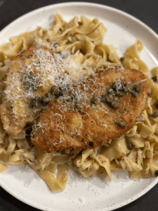 A plate with pasta, chicken, and capers