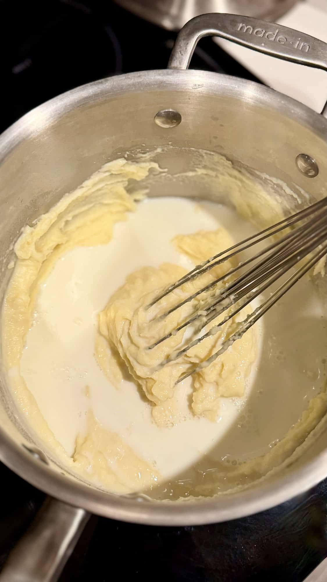 Whisking milk into Béchamel sauce.