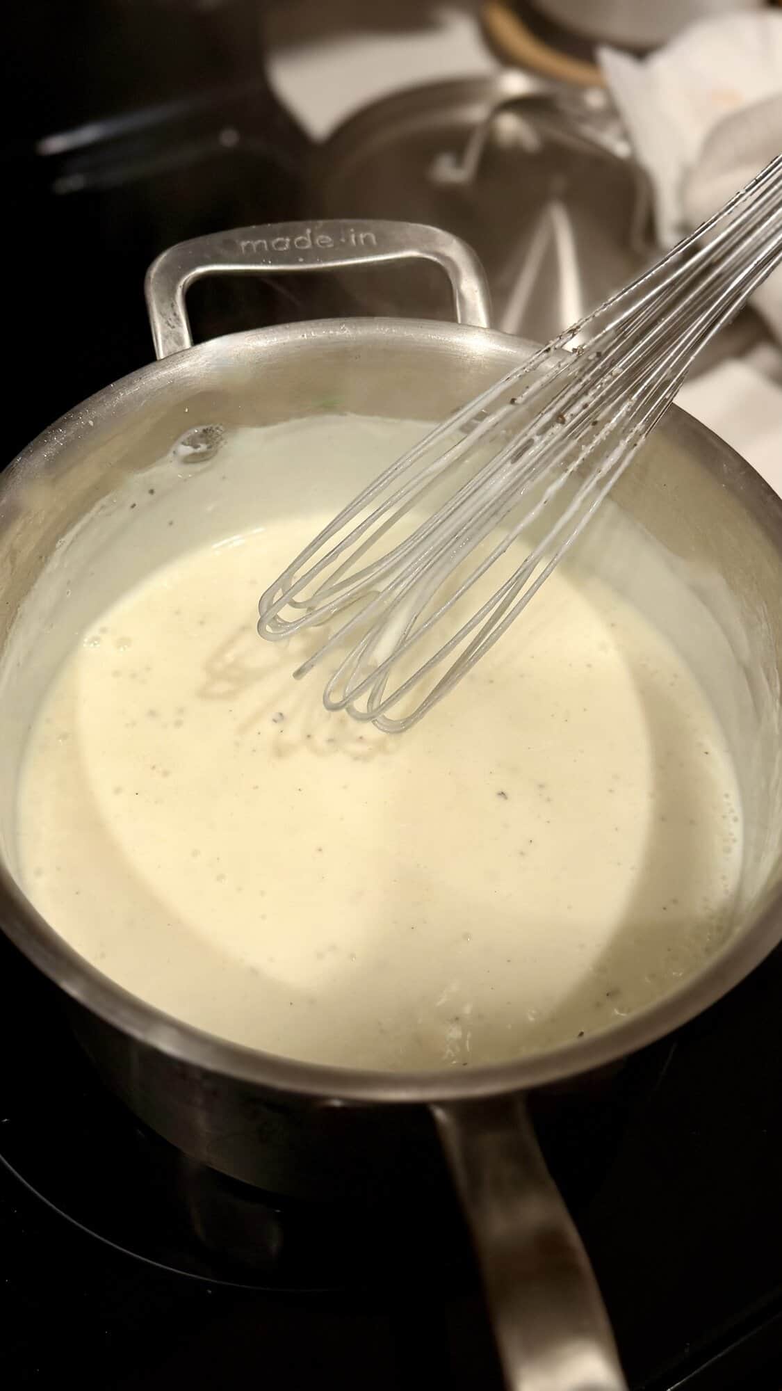 Béchamel sauce thickening over heat on stovetop.
