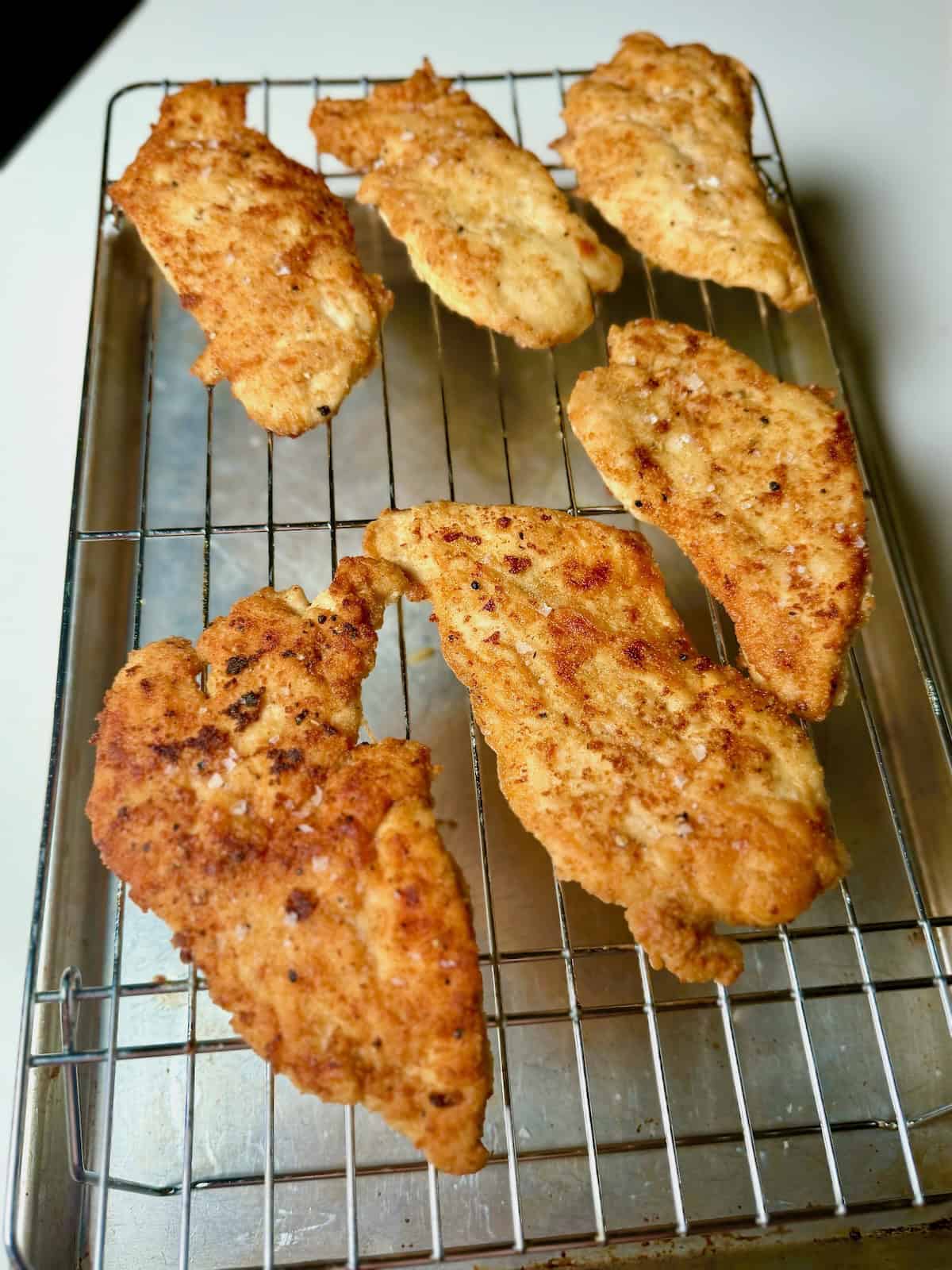 Golden pan-fried chicken cutlets for chicken piccata on wire rack.