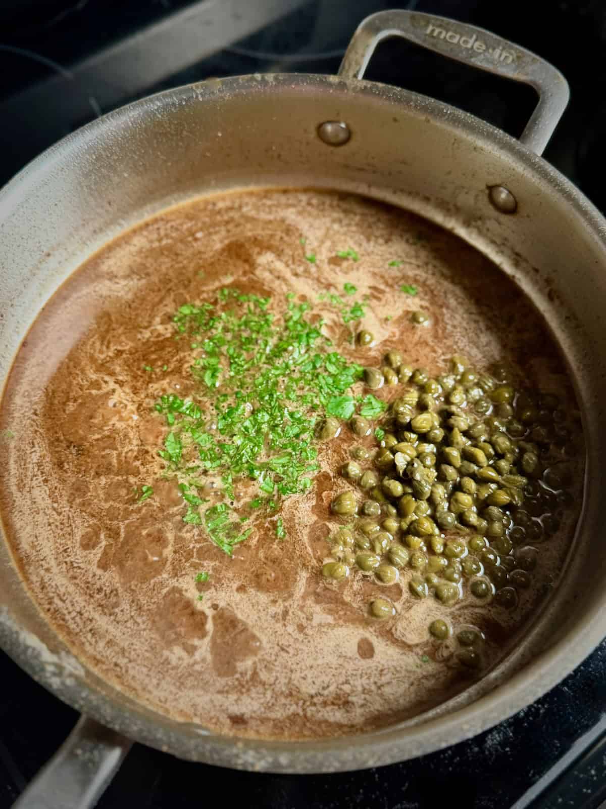 Lemon butter white wine sauce simmering in skillet with capers and parsley for chicken piccata.
